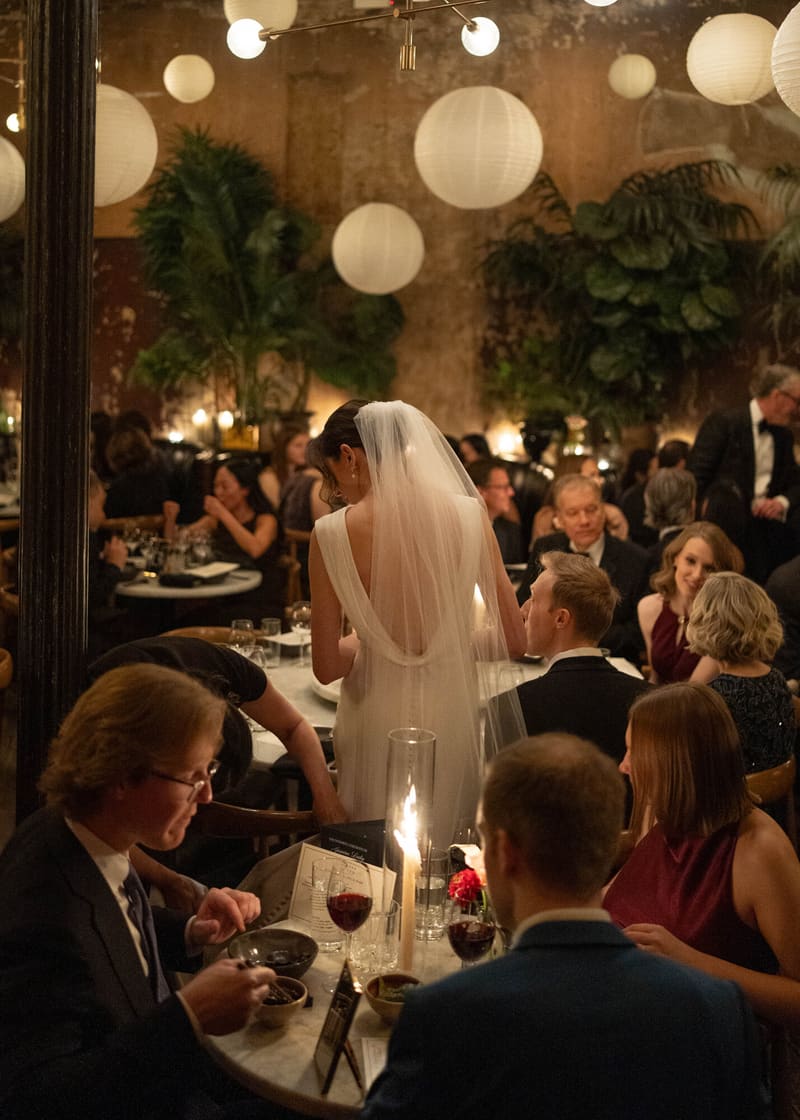 A bride in her veil moving through the candlelit dinner