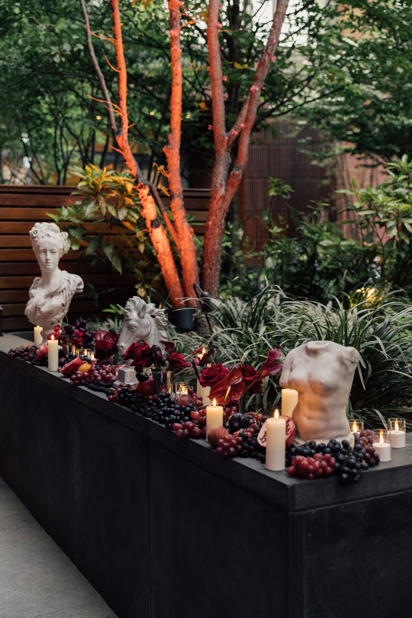 A garden ledge lined with statuary, fruit, and candlelight