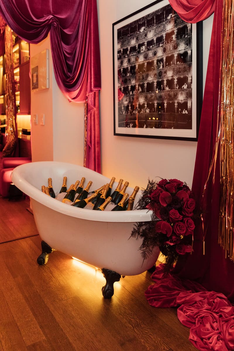 A clawfoot tub filled with ice and champagne beneath red velvet drapes