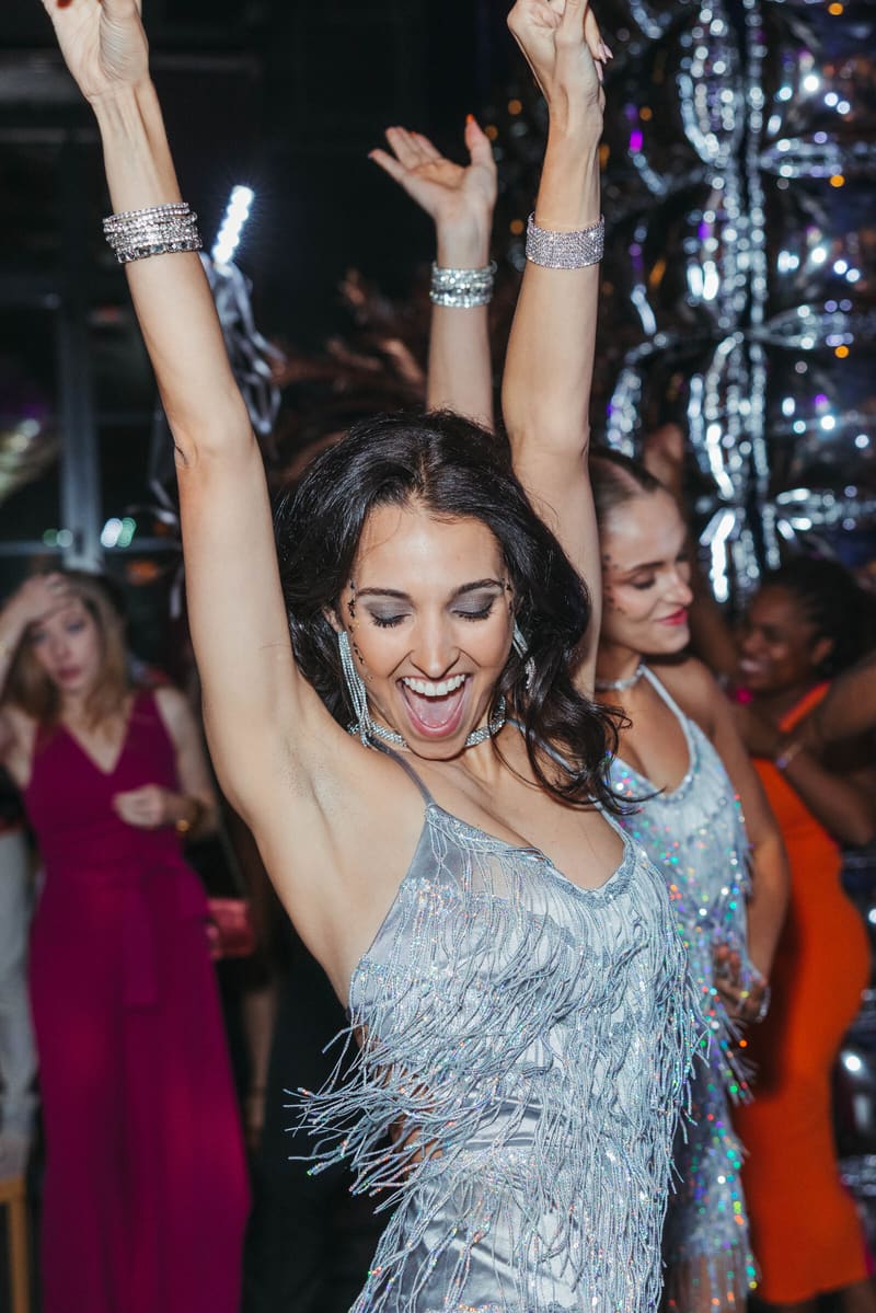 A guest in silver fringe dancing, arms raised