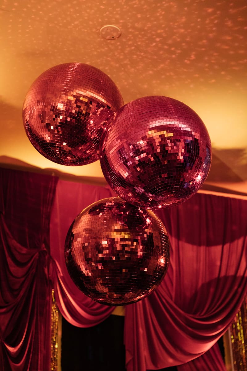 Three pink disco balls under a rose-lit ceiling