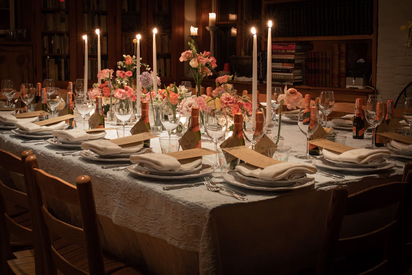 A long candlelit dinner table set with taper candles and pink florals in a library